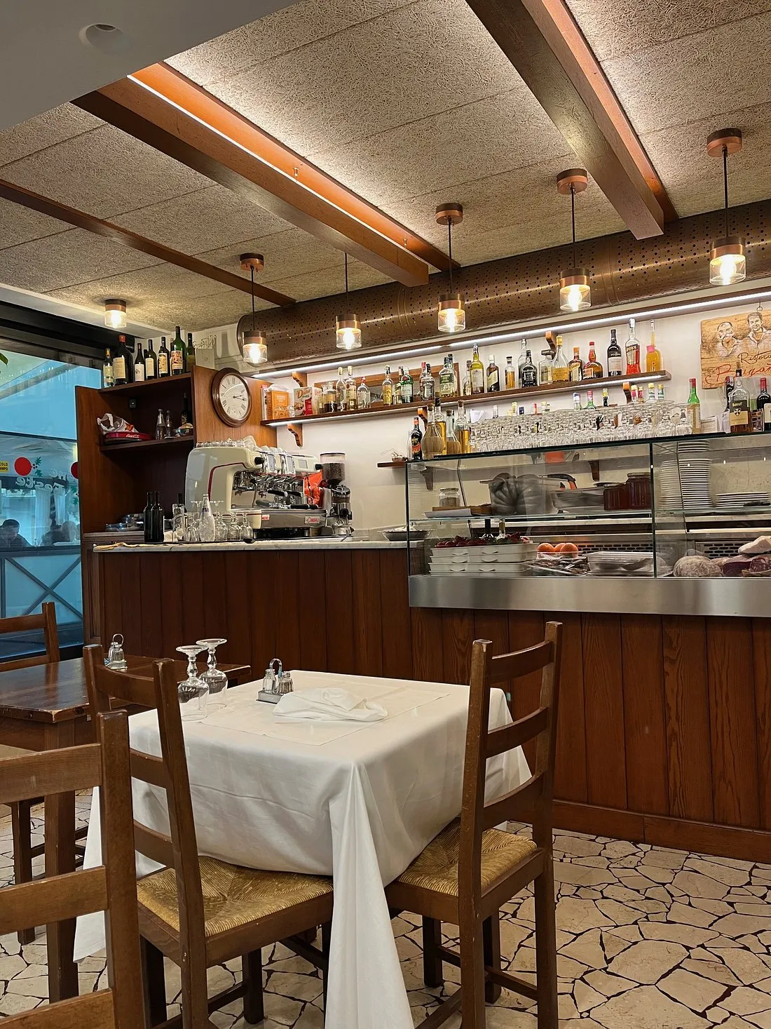 La sala della Trattoria Fratelli Briganti: perlinato di legno, lampade in ottone, tavoli con la tovaglia bianca e la cucina a vista dietro il bancone
